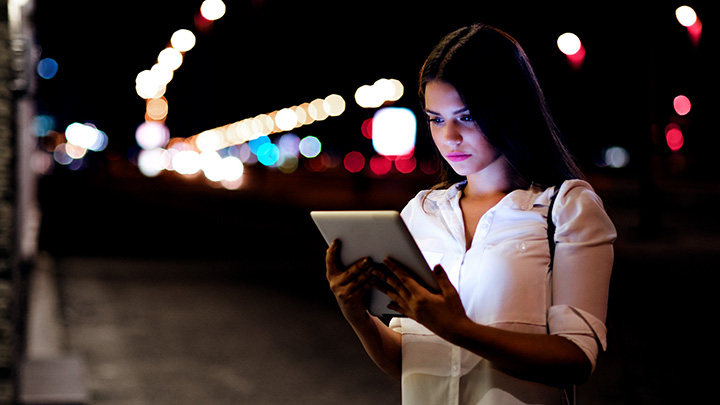 一位女士晚上在城市街道上看平板电脑